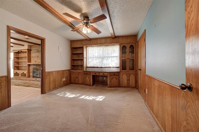 spare room featuring beam ceiling, a ceiling fan, a textured ceiling, wooden walls, and wainscoting