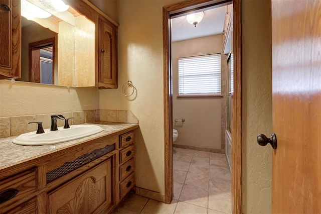 full bathroom with baseboards, toilet, a textured wall, tile patterned floors, and vanity