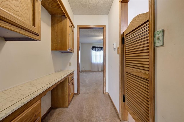 hall with light colored carpet, baseboards, and a textured ceiling