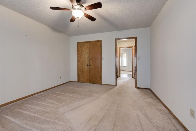 unfurnished bedroom with light carpet, a ceiling fan, a textured ceiling, a closet, and baseboards