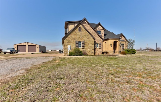 view of front of house with stucco siding, a front lawn, stone siding, an outdoor structure, and a garage