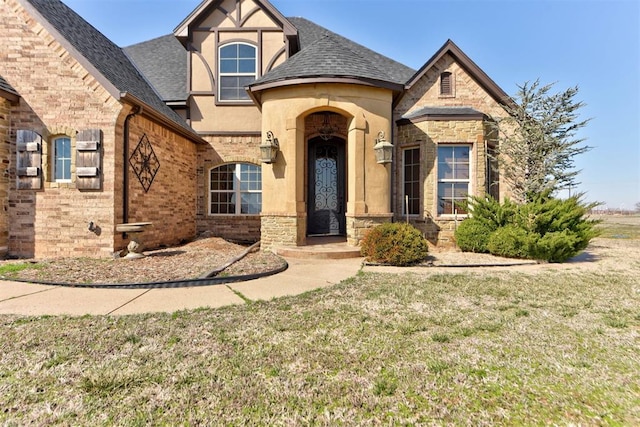 view of front facade with a front lawn, stucco siding, brick siding, and a shingled roof