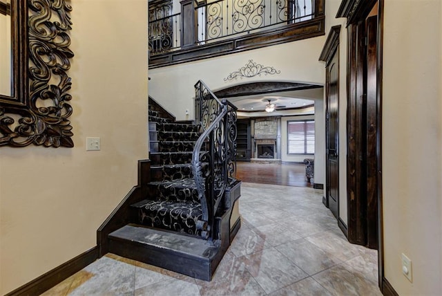 staircase with ceiling fan, baseboards, and a fireplace with raised hearth