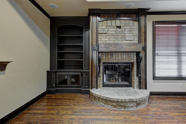 unfurnished living room featuring built in shelves, wood finished floors, a large fireplace, crown molding, and baseboards