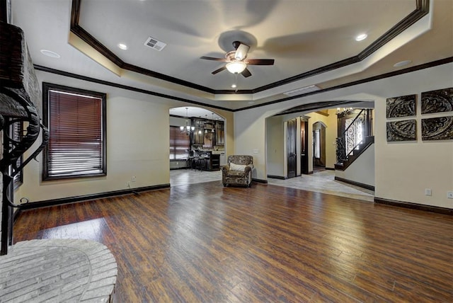 living area featuring a raised ceiling, wood finished floors, ceiling fan with notable chandelier, and arched walkways