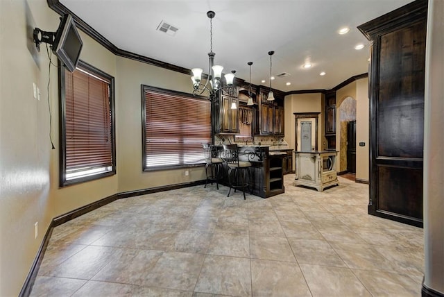 kitchen with baseboards, visible vents, an inviting chandelier, a kitchen bar, and crown molding