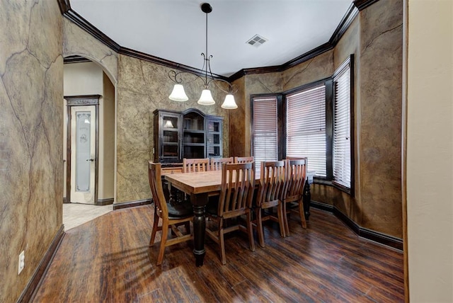 dining space featuring wood finished floors, visible vents, an inviting chandelier, arched walkways, and ornamental molding