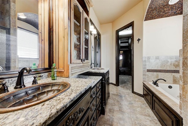 full bathroom featuring a sink, baseboards, a garden tub, and two vanities