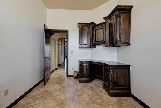 kitchen featuring dark brown cabinets, arched walkways, and baseboards