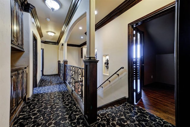 hallway featuring wood finished floors, arched walkways, ornamental molding, and an upstairs landing