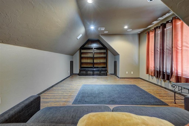 bedroom with visible vents, baseboards, vaulted ceiling, wood finished floors, and a textured ceiling