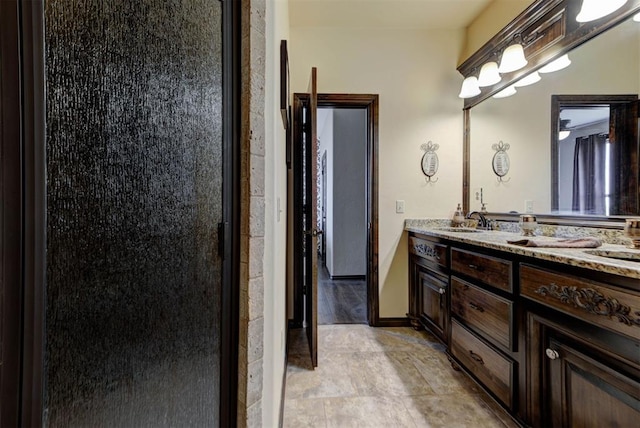 full bath with double vanity, a stall shower, baseboards, and a sink