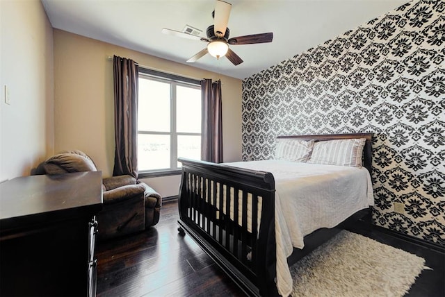 bedroom featuring visible vents, wallpapered walls, an accent wall, ceiling fan, and wood finished floors