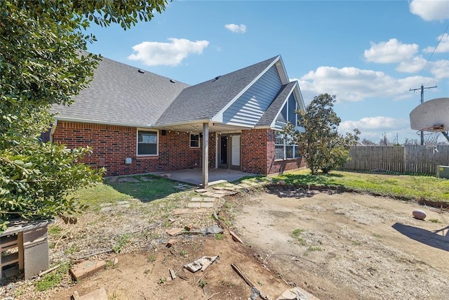 back of house with brick siding, roof with shingles, a patio, and fence