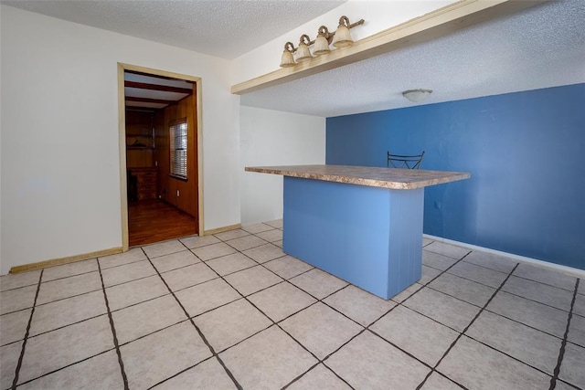 kitchen with light tile patterned floors, a kitchen island, baseboards, and a textured ceiling