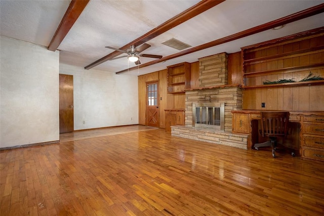 unfurnished living room with visible vents, beam ceiling, wood-type flooring, a stone fireplace, and ceiling fan