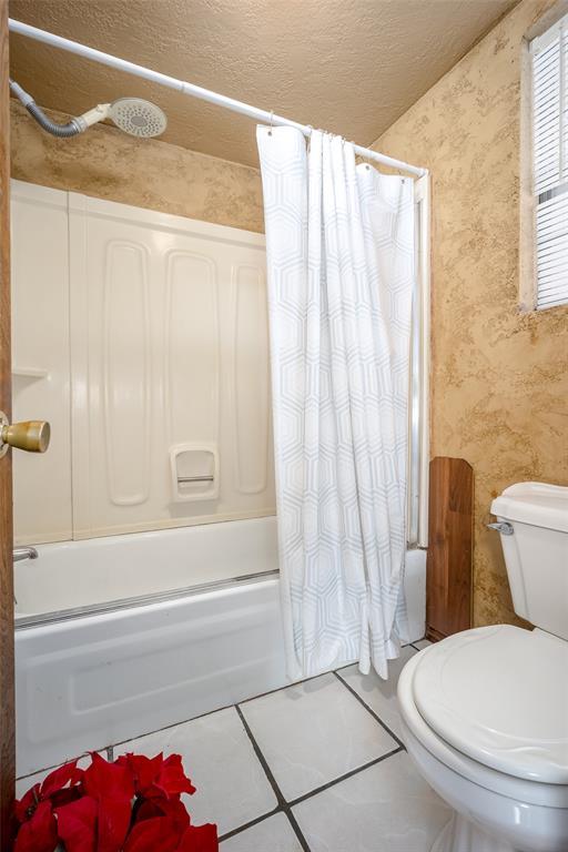 bathroom featuring wallpapered walls, toilet, shower / bath combo with shower curtain, tile patterned floors, and a textured ceiling