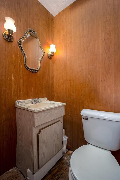 bathroom with wooden walls, toilet, and vanity