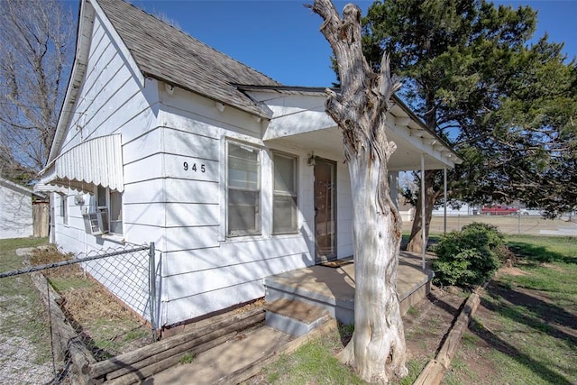 view of home's exterior featuring cooling unit, a porch, roof with shingles, and fence