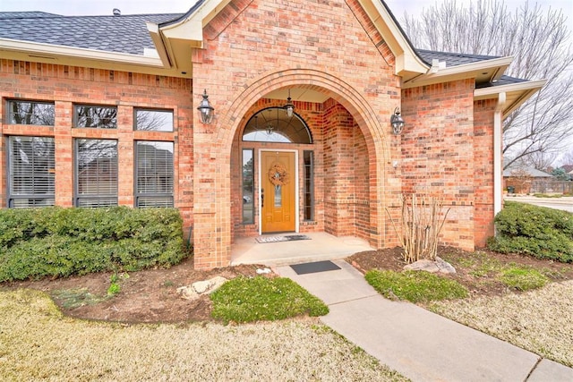 view of exterior entry featuring brick siding and roof with shingles