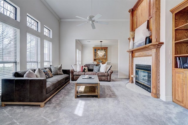 living area featuring carpet floors, a fireplace, ceiling fan, a towering ceiling, and crown molding