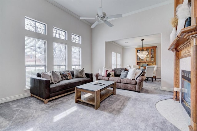 carpeted living room with ceiling fan with notable chandelier, a fireplace, baseboards, and ornamental molding