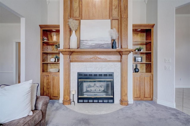 carpeted living room with baseboards, built in shelves, a tiled fireplace, and crown molding