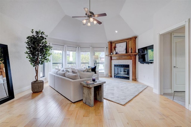 living area featuring baseboards, light wood-style floors, a glass covered fireplace, high vaulted ceiling, and a ceiling fan