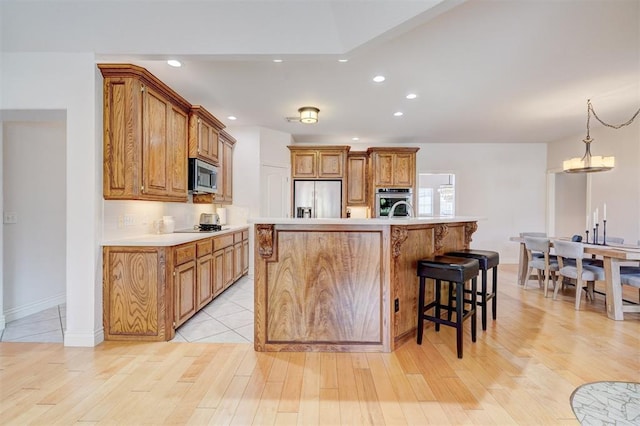 kitchen with appliances with stainless steel finishes, light wood-style flooring, brown cabinetry, and light countertops