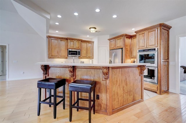 kitchen with appliances with stainless steel finishes, light countertops, light wood-style floors, and a kitchen breakfast bar