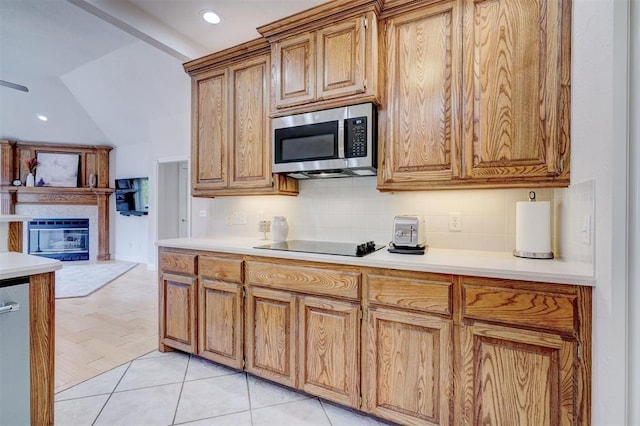 kitchen with stainless steel microwave, light countertops, decorative backsplash, and black electric cooktop