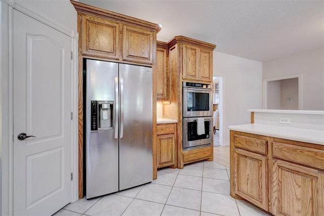 kitchen with light tile patterned floors, stainless steel appliances, brown cabinetry, and light countertops