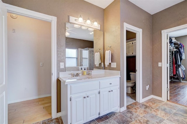 bathroom with baseboards, toilet, a spacious closet, and vanity