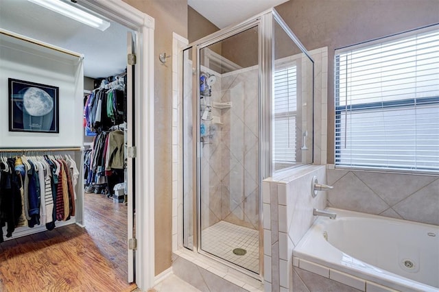 full bath with a walk in closet, wood finished floors, a stall shower, and a whirlpool tub