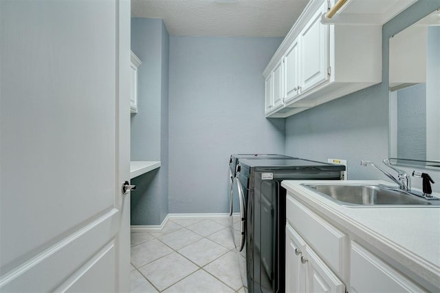 laundry area featuring a sink, cabinet space, light tile patterned floors, baseboards, and washing machine and clothes dryer