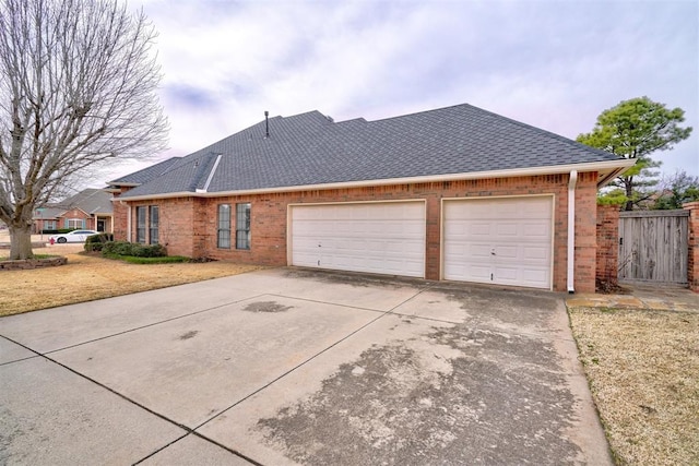 view of side of property with a garage, brick siding, driveway, and a shingled roof