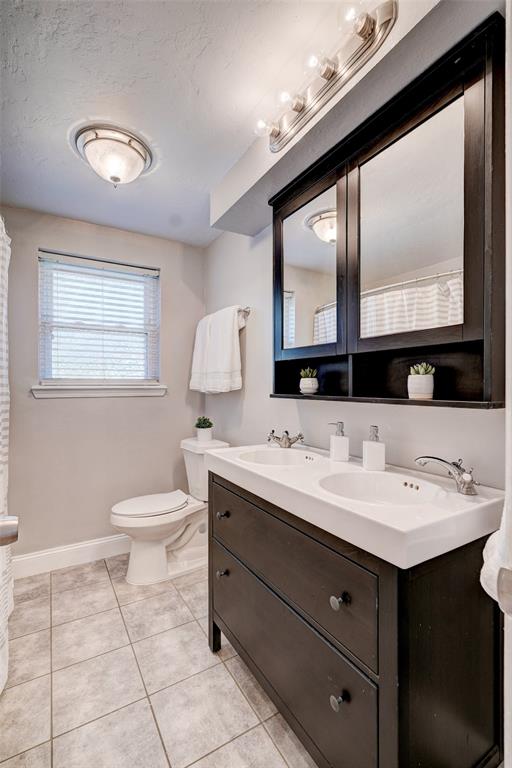 full bathroom featuring baseboards, double vanity, a sink, tile patterned flooring, and toilet