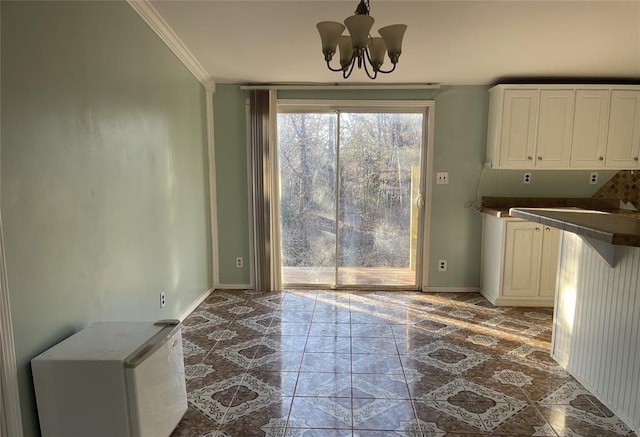 unfurnished dining area featuring tile patterned flooring, an inviting chandelier, baseboards, and ornamental molding