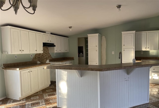 kitchen with white cabinetry, lofted ceiling, dark countertops, and under cabinet range hood