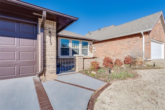 entrance to property featuring brick siding, roof with shingles, and an attached garage