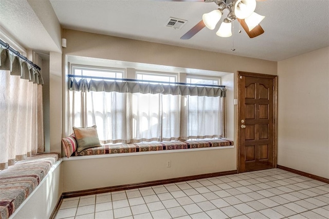 interior space with light tile patterned flooring, visible vents, a ceiling fan, and baseboards