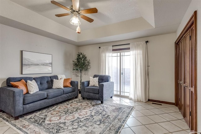 living area featuring light tile patterned floors, ceiling fan, a textured ceiling, and a tray ceiling