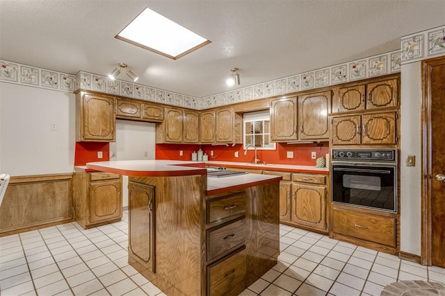 kitchen with oven, brown cabinets, a center island, and light tile patterned floors