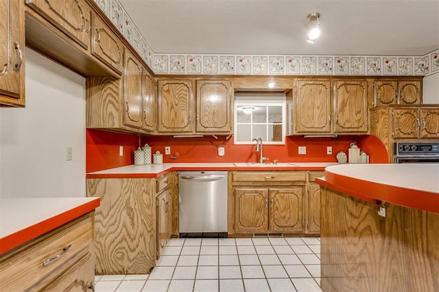 kitchen with brown cabinetry, light countertops, stainless steel dishwasher, light tile patterned flooring, and a sink