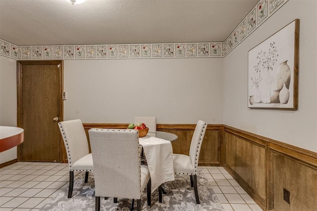 dining room with light tile patterned floors, a wainscoted wall, and a textured ceiling