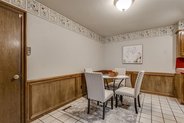 dining space featuring light tile patterned floors, wainscoting, and a textured ceiling