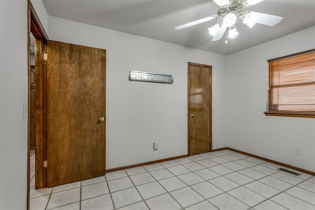 empty room featuring light tile patterned floors, visible vents, baseboards, and ceiling fan