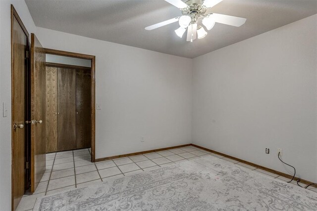 unfurnished bedroom with a textured ceiling, light tile patterned floors, baseboards, and ceiling fan