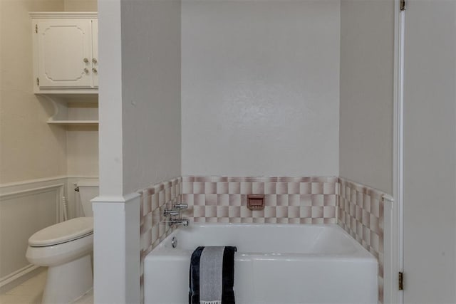 full bathroom with a wainscoted wall, toilet, a bath, and a decorative wall