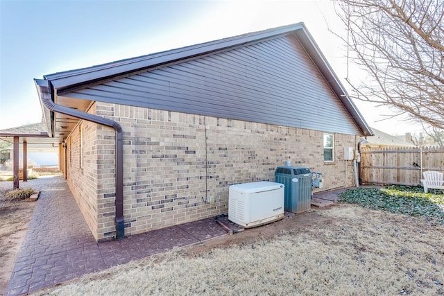 view of property exterior with cooling unit, fence, and brick siding